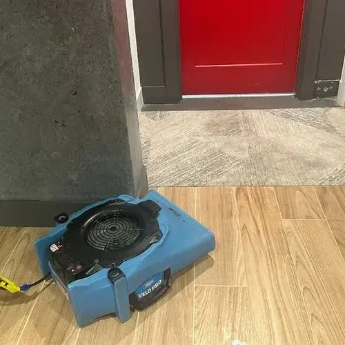 An air mover drying a wood-look tile floor beside an open doorway