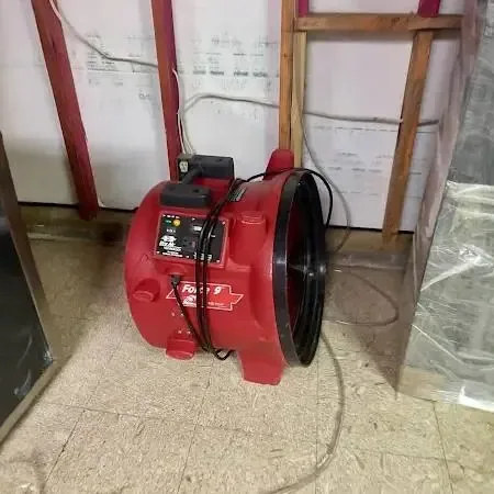 A red air mover drying a room with the lower wall opened and plastic sheeting hung