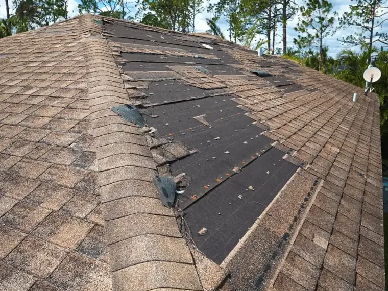 Wind-stripped shingles exposing roof underlayment after a storm